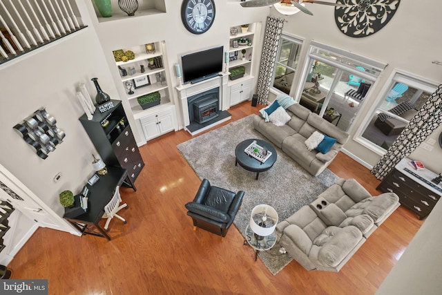 11742 Maid At Arms Ln, Berlin, MD 21811 - living room with wood finished floors, built in shelves, a ceiling fan, a high ceiling, and a warm lit fireplace