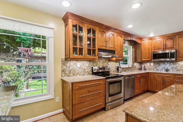 8600 Fox Run, Potomac, MD 20854 - kitchen with stainless steel appliances, under cabinet range hood, light stone counters, glass insert cabinets, and light tile patterned flooring