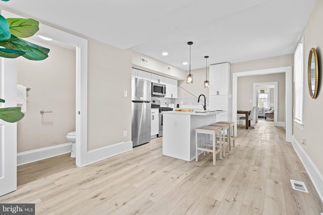 3414 Old York Rd, Baltimore, MD 21218 - kitchen with appliances with stainless steel finishes, light wood-style flooring, white cabinets, a kitchen bar, and decorative backsplash