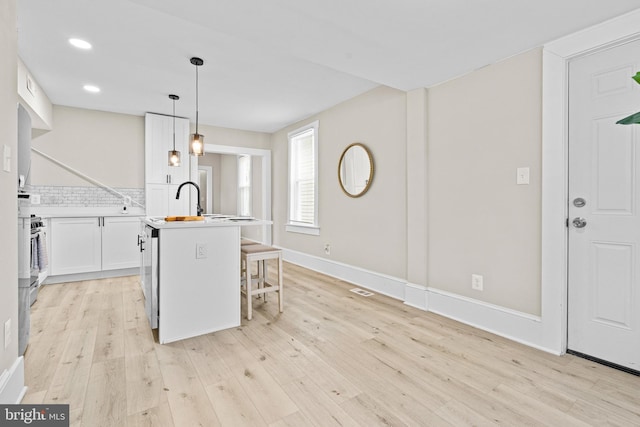 3414 Old York Rd, Baltimore, MD 21218 - kitchen with light wood-style floors, a center island with sink, white cabinets, a kitchen bar, and pendant lighting