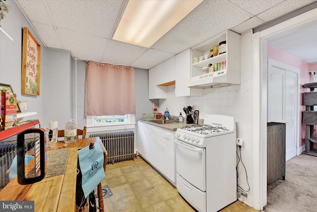 133 S Prospect Ave, Baltimore, MD 21228 - kitchen with white gas range oven, radiator, a paneled ceiling, under cabinet range hood, and white cabinetry