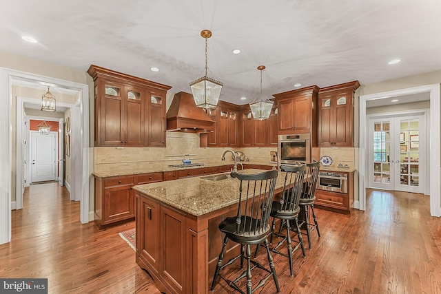 217 Valley Ridge Rd, Haverford, PA 19041 - kitchen with custom exhaust hood, appliances with stainless steel finishes, wood finished floors, light stone counters, and glass insert cabinets