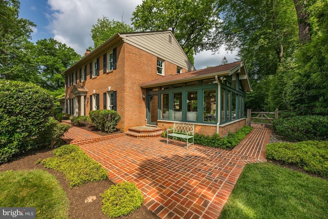 9017 Rouen Ln, Potomac, MD 20854 - rear view of house featuring a sunroom, brick siding, a patio, and a chimney