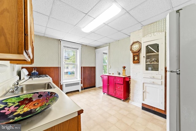 73 Fairfield Ave, Lawrence, NJ 08648 - kitchen with wallpapered walls, radiator heating unit, light floors, freestanding refrigerator, and a drop ceiling