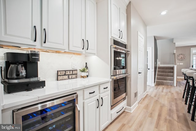18510 Barton Creek Pl, Leesburg, VA 20176 - kitchen featuring stainless steel double oven, wine cooler, white cabinets, light stone counters, and light wood-type flooring