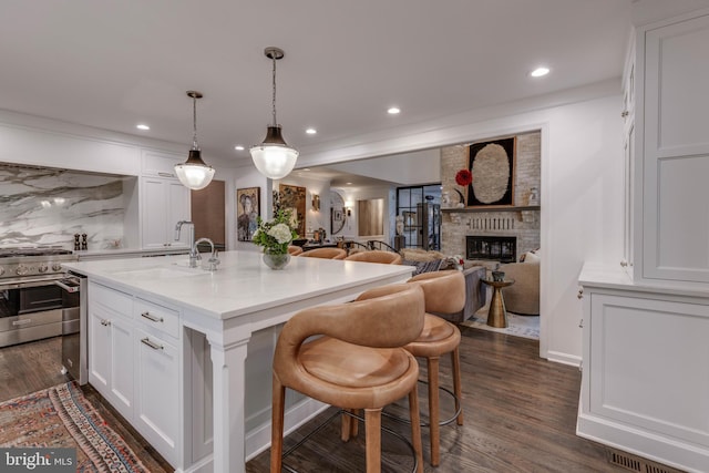 8 Rockland Vue Ct, Towson, MD 21204 - kitchen with stainless steel stove, white cabinetry, a brick fireplace, recessed lighting, and an island with sink