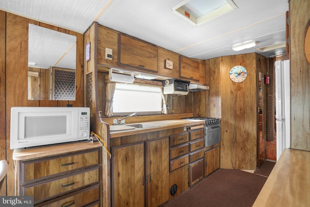 8096 Mire Pond One, Chincoteague Island, VA 23336 - kitchen with white appliances, wood walls, brown cabinetry, under cabinet range hood, and butcher block counters