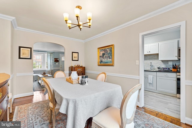 222 Blakeney Rd, Baltimore, MD 21228 - dining area featuring arched walkways, a chandelier, light wood finished floors, and ornamental molding