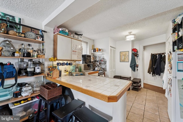 3 W Gowen Ave, Philadelphia, PA 19119 - kitchen with tile counters, a textured ceiling, a peninsula, a kitchen breakfast bar, and light tile patterned floors