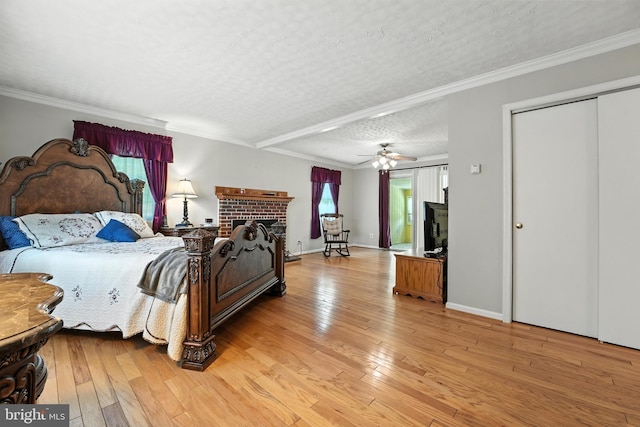 bedroom featuring light wood-style flooring, a textured ceiling, a brick fireplace, and ornamental molding