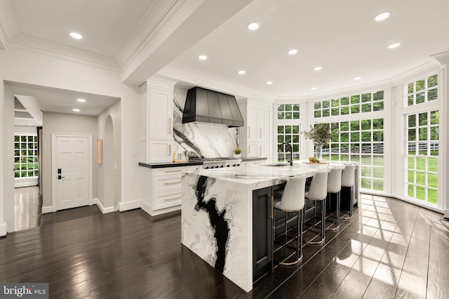 13300 Manor Stone Dr, Darnestown, MD 20874 - kitchen with premium range hood, ornamental molding, a center island with sink, white cabinetry, and light stone counters
