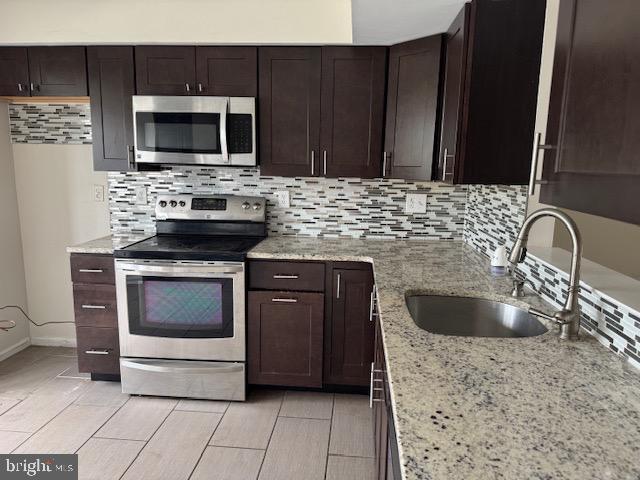 7849 Hidden Crk Unit 24, Baltimore, MD 21226 - kitchen featuring appliances with stainless steel finishes, tasteful backsplash, a sink, and light stone countertops