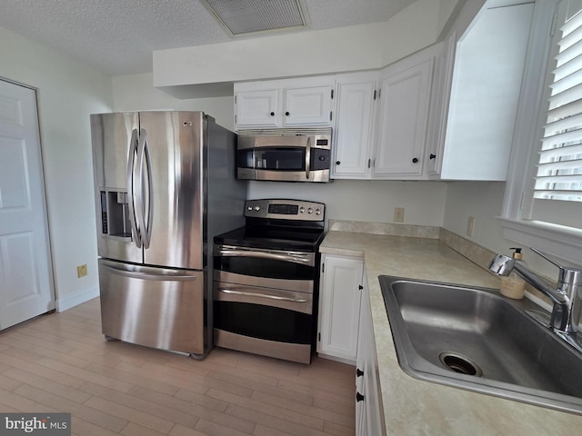 156 Captains Quarters Rd, Ocean City, MD 21842 - kitchen with appliances with stainless steel finishes, light countertops, white cabinetry, light wood-style floors, and a textured ceiling