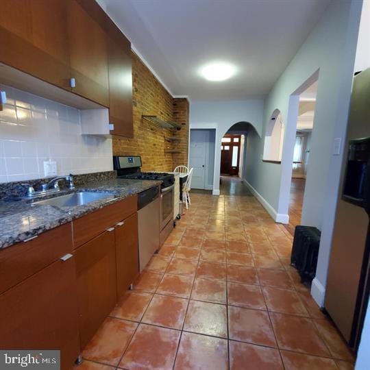 1212 Park Rd NW, Washington, DC 20010 - kitchen with stainless steel appliances, arched walkways, light tile patterned floors, brown cabinetry, and decorative backsplash