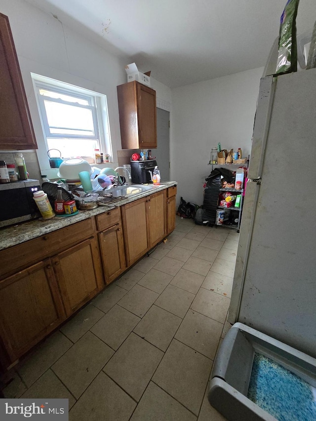 2513 W Sergeant St, Philadelphia, PA 19132 - kitchen with stainless steel microwave, freestanding refrigerator, light countertops, light tile patterned floors, and brown cabinets