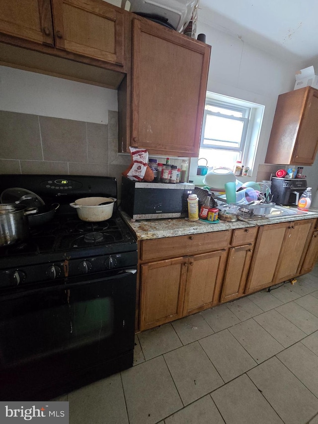 2513 W Sergeant St, Philadelphia, PA 19132 - kitchen with black gas range oven, backsplash, light tile patterned flooring, brown cabinets, and light stone countertops