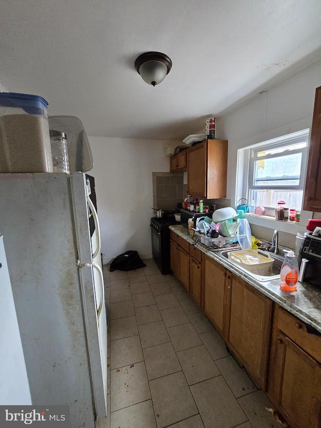 2513 W Sergeant St, Philadelphia, PA 19132 - kitchen featuring black gas range oven, freestanding refrigerator, brown cabinets, and light tile patterned floors