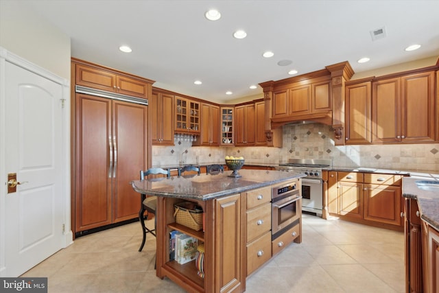 2573 Muirfield Way, Lansdale, PA 19446 - kitchen with high end appliances, brown cabinets, dark stone counters, light tile patterned floors, and decorative backsplash