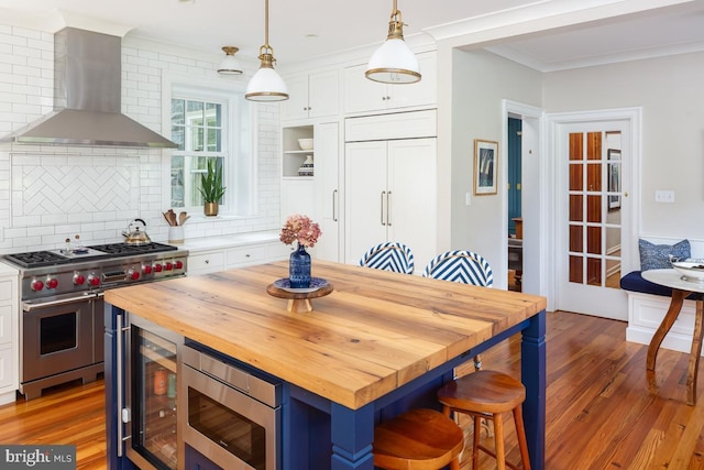 673 Ardmore Ave, Ardmore, PA 19003 - kitchen with wall chimney exhaust hood, stainless steel appliances, butcher block countertops, white cabinets, and ornamental molding