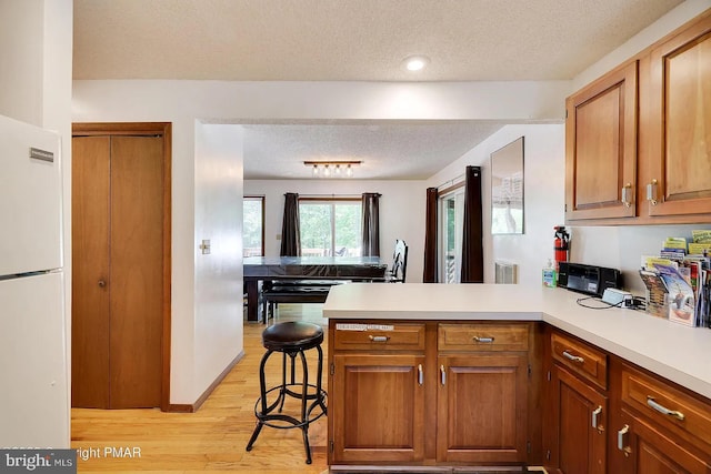138 Banbury Dr, Bushkill, PA 18324 - kitchen featuring a textured ceiling, freestanding refrigerator, a peninsula, light wood finished floors, and light countertops