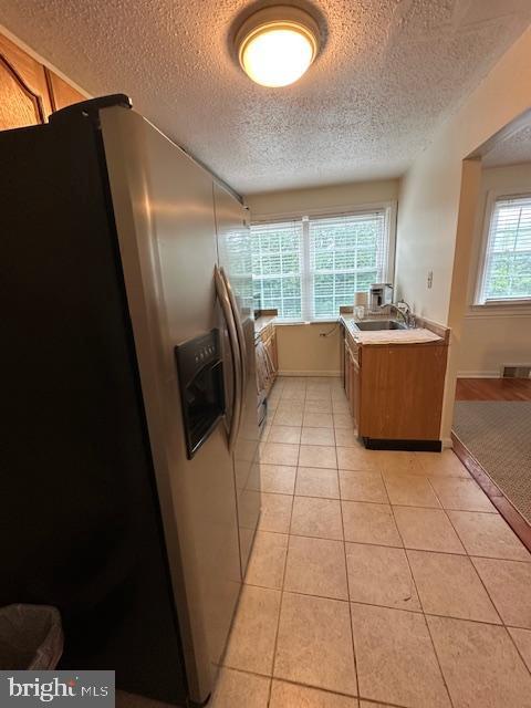 710 Wildell Rd Unit 108, Drexel Hill, PA 19026 - kitchen featuring stainless steel refrigerator with ice dispenser, a textured ceiling, light tile patterned floors, light countertops, and brown cabinets