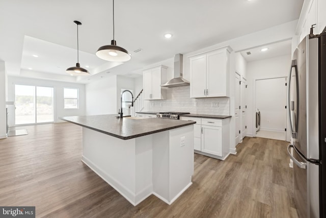 19740 Spinnaker Ct, Georgetown, DE 19947 - kitchen with stainless steel appliances, wall chimney exhaust hood, dark countertops, light wood finished floors, and a sink
