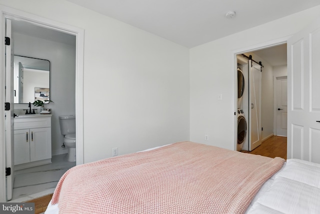 2127 12th Pl NW, Washington, DC 20009 - bedroom featuring stacked washer / drying machine, a barn door, ensuite bathroom, and wood finished floors