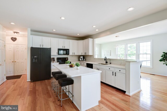 213 Casper Way, Middletown, DE 19709 - kitchen with black appliances, a peninsula, a breakfast bar, white cabinets, and light wood-style floors