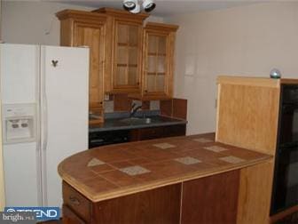 kitchen featuring white fridge with ice dispenser, glass insert cabinets, and brown cabinetry
