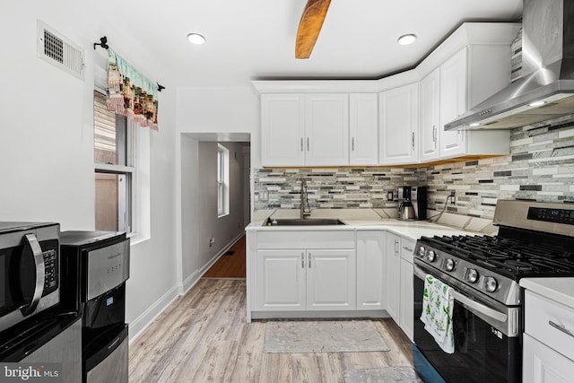1228 S 22nd St, Philadelphia, PA 19146 - kitchen featuring wall chimney exhaust hood, stainless steel appliances, tasteful backsplash, light wood-style floors, and white cabinets