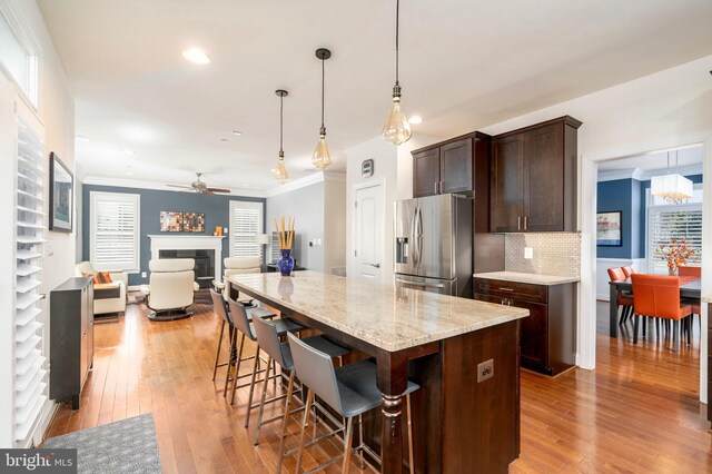 6139 Sligo Mill Rd NE, Washington, DC 20011 - kitchen with stainless steel fridge, dark brown cabinetry, light wood-style floors, a glass covered fireplace, and a kitchen bar