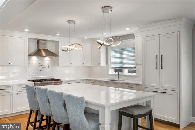 1005 Dune Dr, Avalon, NJ 08202 - kitchen with wall chimney range hood, white cabinetry, a breakfast bar area, light countertops, and recessed lighting