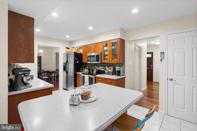 14519 Keeneland Cir, North Potomac, MD 20878 - kitchen featuring stainless steel appliances, brown cabinetry, light tile patterned floors, glass insert cabinets, and backsplash