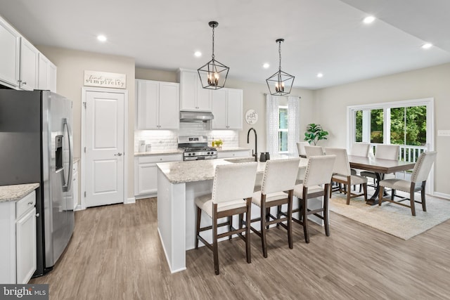 57 Oak Ln, Carneys Point, NJ 08069 - kitchen featuring appliances with stainless steel finishes, under cabinet range hood, light wood-style flooring, tasteful backsplash, and an island with sink