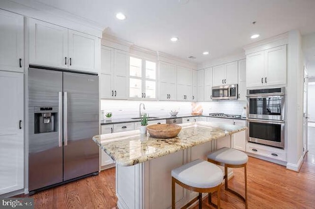409 S Henry St, Alexandria, VA 22314 - kitchen with stainless steel appliances, white cabinets, light wood-type flooring, a kitchen breakfast bar, and backsplash