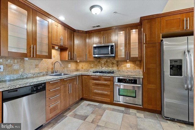 326 Brickhouse Rd, Princeton, NJ 08540 - kitchen with stainless steel appliances, decorative backsplash, light stone counters, brown cabinetry, and glass insert cabinets