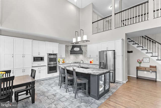 43251 Brownstone Ct, Ashburn, VA 20147 - kitchen featuring stainless steel appliances, a towering ceiling, white cabinets, a kitchen island with sink, and pendant lighting