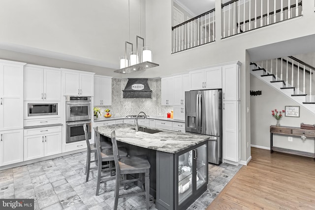 43251 Brownstone Ct, Ashburn, VA 20147 - kitchen featuring stainless steel appliances, white cabinetry, a towering ceiling, an island with sink, and light stone counters