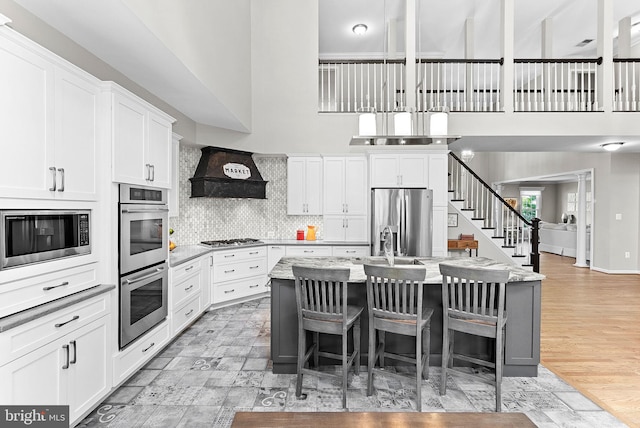 43251 Brownstone Ct, Ashburn, VA 20147 - kitchen with stainless steel appliances, custom exhaust hood, a kitchen island with sink, a high ceiling, and white cabinets