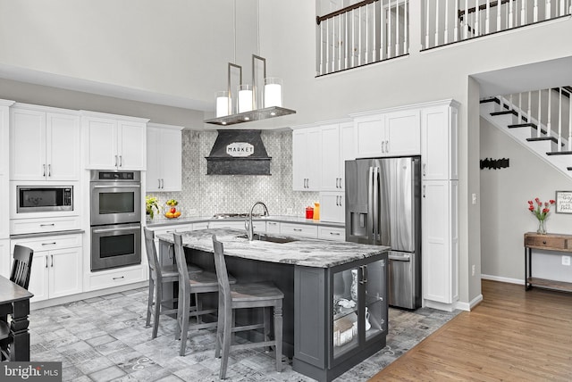 43251 Brownstone Ct, Ashburn, VA 20147 - kitchen featuring stainless steel appliances, a high ceiling, white cabinets, ventilation hood, and a center island with sink