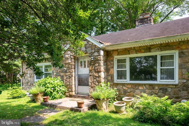 214 Sugartown Rd, Devon, PA 19333 - view of exterior entry with stone siding, a chimney, a yard, and a shingled roof