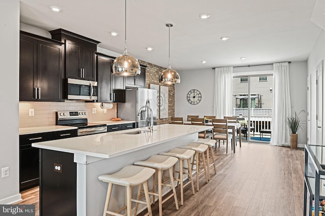 1036 Cantina Ter SE, Leesburg, VA 20175 - kitchen with stainless steel appliances, an island with sink, light wood-style flooring, decorative backsplash, and a breakfast bar