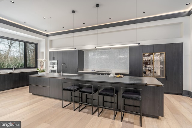 1020 Langley Hill Dr, Mclean, VA 22101 - kitchen featuring modern cabinets, light wood-type flooring, backsplash, a breakfast bar, and dark countertops