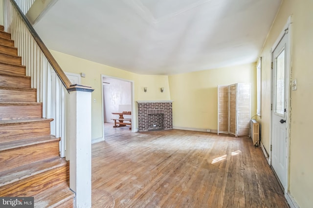 2704 N Tatnall St, Wilmington, DE 19802 - unfurnished living room featuring stairs, radiator heating unit, wood finished floors, and a brick fireplace