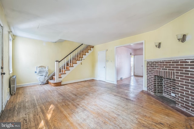 2704 N Tatnall St, Wilmington, DE 19802 - unfurnished living room with radiator heating unit, wood finished floors, stairs, and a brick fireplace