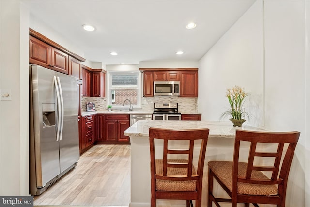 575 Wanamaker Rd, Jenkintown, PA 19046 - kitchen featuring stainless steel appliances, light wood finished floors, decorative backsplash, reddish brown cabinets, and a kitchen bar