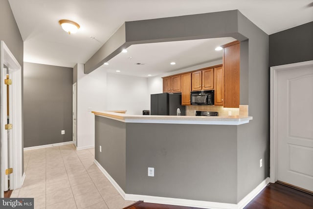 9710 Handerson Pl Unit 1, Manassas Park, VA 20111 - kitchen with black appliances, brown cabinetry, decorative backsplash, light countertops, and a peninsula