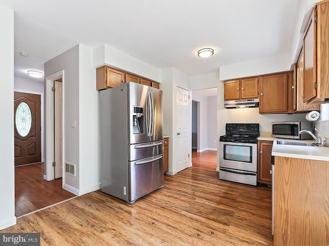 1035 Deerfield Cir, Perkasie, PA 18944 - kitchen with stainless steel appliances, under cabinet range hood, light countertops, wood finished floors, and brown cabinetry