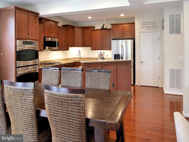15152 Santander Dr, Gainesville, VA 20155 - kitchen featuring appliances with stainless steel finishes, wood finished floors, recessed lighting, brown cabinets, and light stone countertops