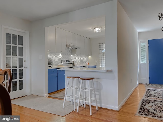 12987 Holly Way, Lusby, MD 20657 - kitchen featuring blue cabinetry, light wood finished floors, a breakfast bar, under cabinet range hood, and backsplash